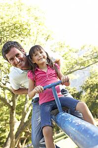 Father And Daughter Riding On See Saw In Playground