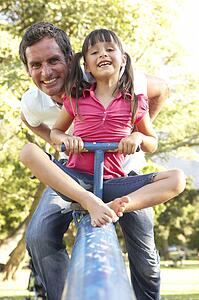 Father And Daughter Riding On See Saw In Playground