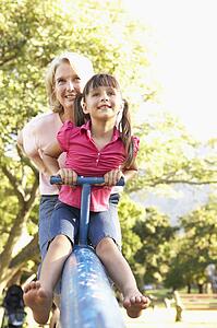 Grandmother And Granddaughter Riding On See Saw In Playground