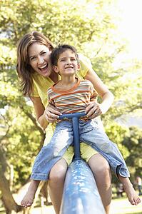 Mother And Son Riding On See Saw In Playground