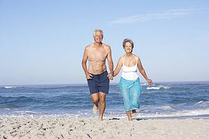 Senior Couple On Holiday Running Along Sandy Beach