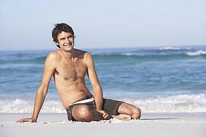 Young ManWearing Swimwear Sitting On Sandy Beach