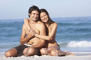 Young Couple Relaxing On Beach Wearing Swimwear
