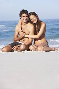 Young Couple Relaxing On Beach Wearing Swimwear