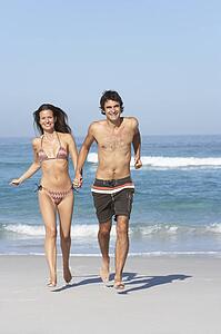 Young Couple Running On Beach Wearing Swimwear