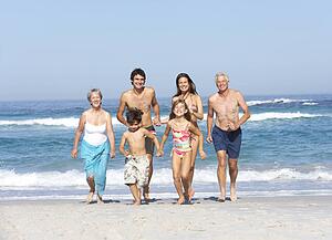 Three Generation Family On Holiday Walking Along Beach