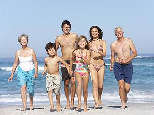 Three Generation Family On Holiday Walking Along Beach