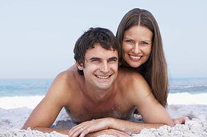 Young Couple Relaxing On Beach Wearing Swimwear