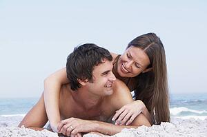 Young Couple Relaxing On Beach Wearing Swimwear