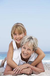 Grandmother Relaxing On Sandy Beach With Granddaughter
