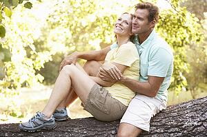 Young Couple In Walking Clothes Resting On Tree In Park
