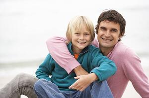 Father And Son Sitting On Winter Beach Together
