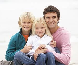 Father And Children Sitting On Winter Beach Together