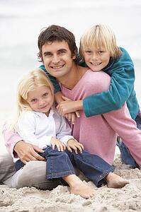 Father And Children Sitting On Winter Beach Together