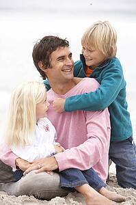 Father And Children Sitting On Winter Beach Together