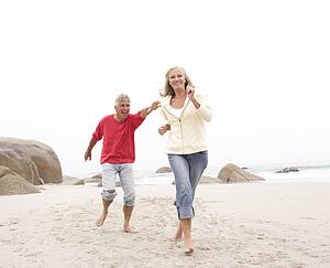 Senior Couple On Holiday Running Along Winter Beach
