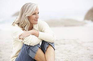 Senior Woman On Holiday Sitting On Winter Beach