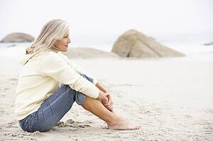 Senior Woman On Holiday Sitting On Winter Beach
