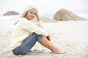 Senior Woman On Holiday Sitting On Winter Beach