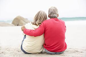 Senior Couple On Holiday Sitting On Winter Beach