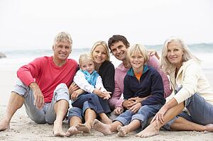 Three Generation Family Sitting On Winter Beach Together