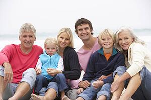 Three Generation Family Sitting On Winter Beach Together