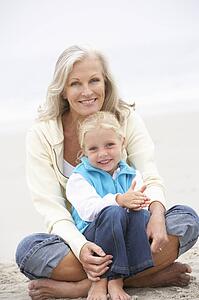 Grandmother And Granddaughter On Holiday Sitting On Winter Beach