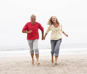 Senior Couple On Holiday Running Along Winter Beach