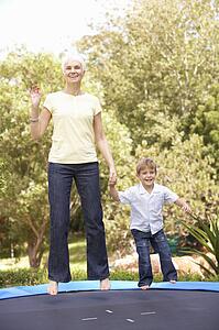 Grandmother And Grandson Jumping On Trampoline In Garden