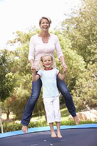 Mother And Daughter Jumping On Trampoline In Garden