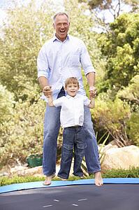 Father And Son Jumping On Trampoline In Garden