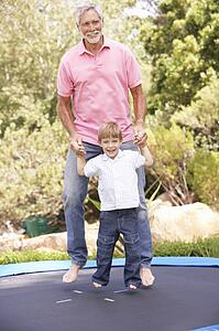 Grandfather And Grandson Jumping On Trampoline In Garden