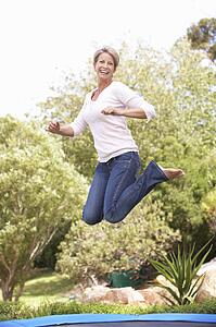 Woman Jumping On Trampoline In Garden