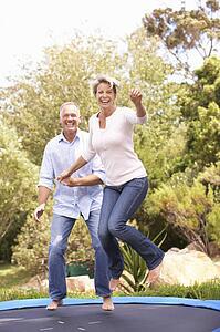 Couple Jumping On Trampoline In Garden