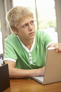 Guilty Looking Teenage Boy Using Laptop At Home