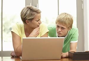Mother And Teenage Son Using Laptop At Home