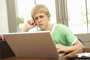 Worried Looking Teenage Boy Using Laptop At Home