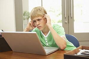 Worried Looking Teenage Boy Using Laptop At Home