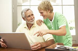 Teenage Grandson Helping Grandfather To Use Laptop At Home