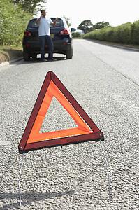 Driver Broken Down On Country Road With Hazard Warning Sign In Foreground