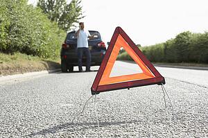 Driver Broken Down On Country Road With Hazard Warning Sign In Foreground