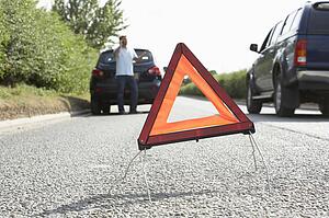 Driver Broken Down On Country Road With Hazard Warning Sign In Foreground