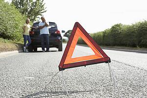 Couple Broken Down On Country Road With Hazard Warning Sign In Foreground