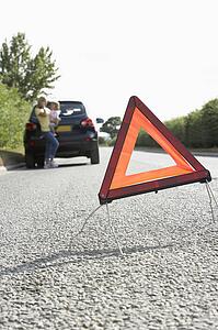Mother And Daughter Broken Down On Country Road With Hazard Warning Sign In Foreground