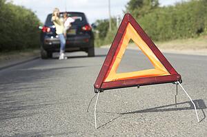Mother And Daughter Broken Down On Country Road With Hazard Warning Sign In Foreground