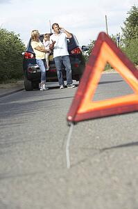 Family Broken Down On Country Road With Hazard Warning Sign In Foreground