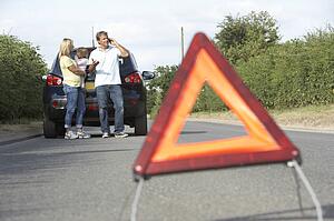 Family Broken Down On Country Road With Hazard Warning Sign In Foreground