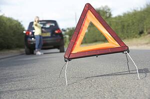 Female Driver Broken Down On Country Road With Hazard Warning Sign In Foreground