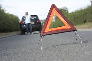 Driver Broken Down On Country Road With Hazard Warning Sign In Foreground