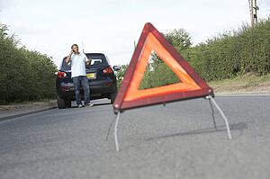 Driver Broken Down On Country Road With Hazard Warning Sign In Foreground